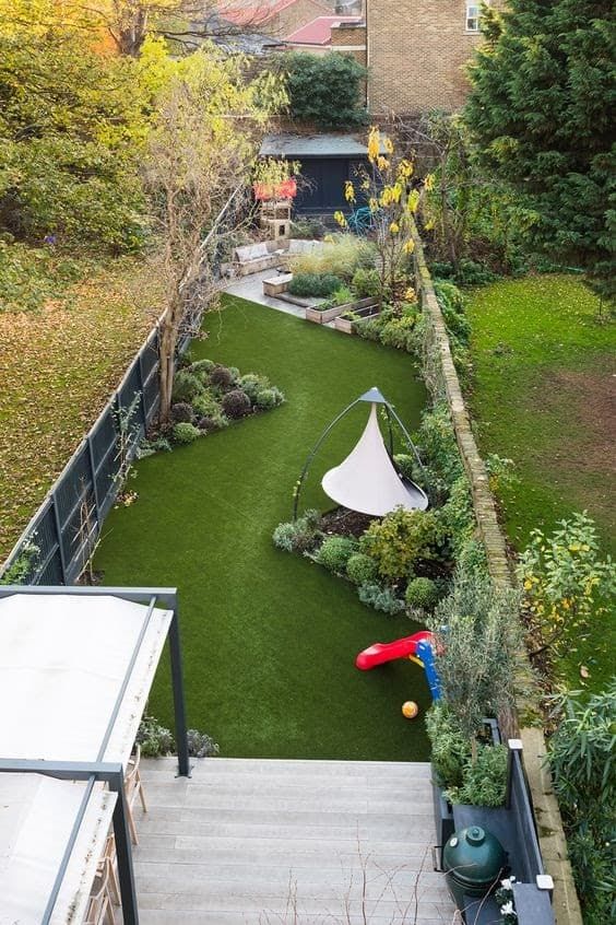 a long and narrow backyard featuring a grene lawn, some shrubs and trees, garden furniture and a stepped deck