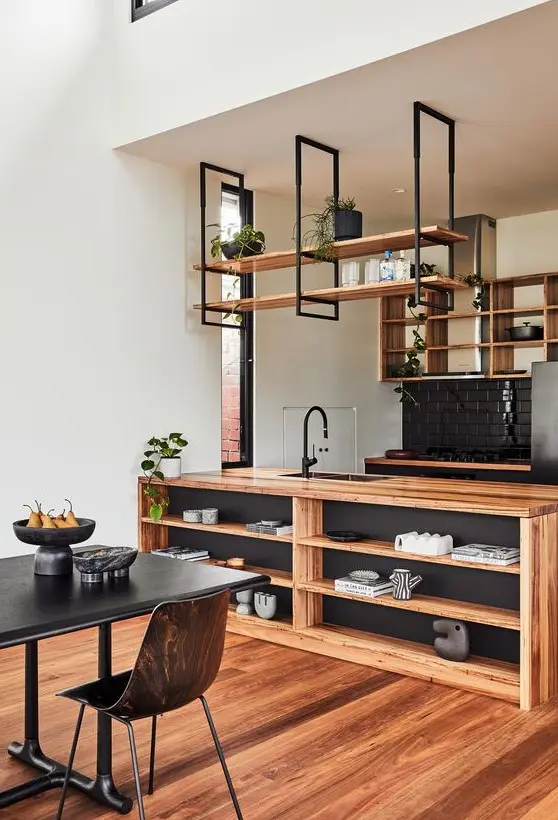 A stylish kitchen in black and light stained wood, with open cabinets and suspended shelves, a storage kitchen island and potted greenery