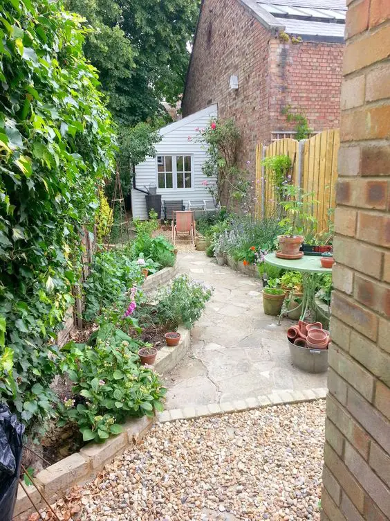 a long and narrow garden clad with stone, with raised garden beds with bold blooms and greenery is a lovely space