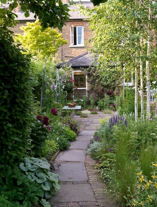 a cute narrow garden with a tile pathway, greenery and blooms is a dreamy space with a dining set