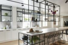 19 an airy kitchen with white cabinets and a large kitchen island, black metal and glass suspended shelves and ablack stools