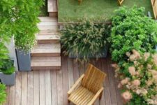 25 a small modern backyard with a raised platform with grass and a lounger, with potted trees, a ladder and a wooden deck with some wooden furniture