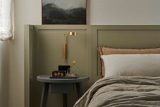 25 an elegant bedroom with olive green paneling, a bed with olive green and neutral bedding, a grey nightstand and a gold sconce