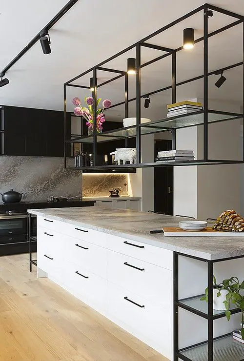 A contemporary kitchen with black cabinets, a white kitchen island, suspended shelves over the island and built in lights