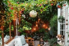 28 a very cozy small backyard with lots of greenery and blooms, lights, paper lamps and some comfy furniture