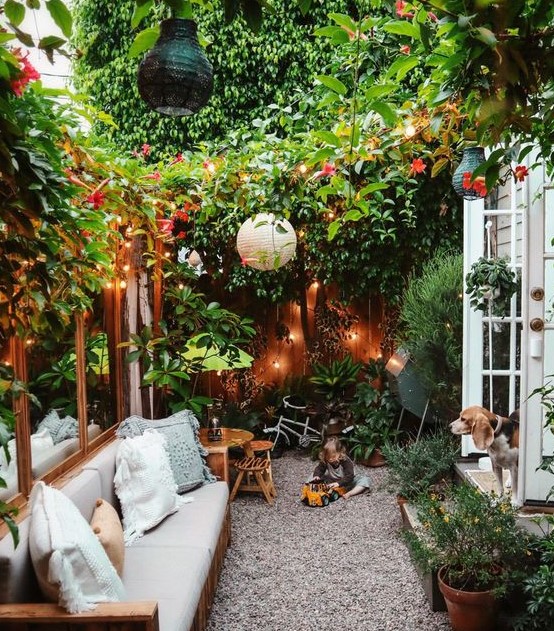 a very cozy small backyard with lots of greenery and blooms, lights, paper lamps and some comfy furniture