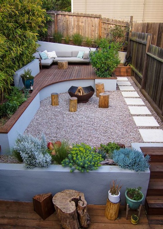 an ultra-modern backyard with a wooden deck with furniture, concrete planters, tree stumps and a fire pit