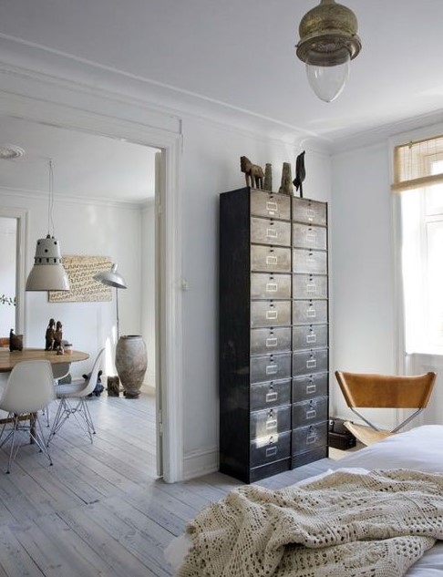 A light filled Scandinavian space with a dark card cabinet that is used instead of a usual dresser and a leather chair
