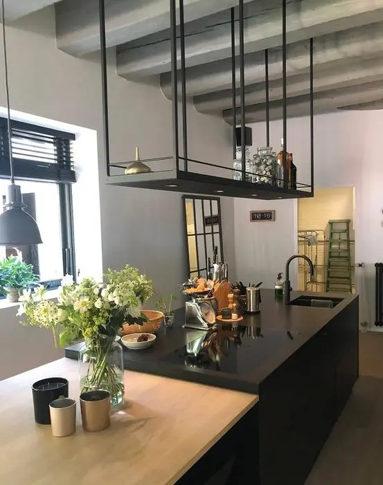 a minimalist kitchen with a black kitchen island and a black suspended shelf over it, with greenery and suspended lamps