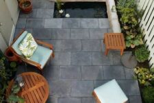 32 a small and zen-like paved patio with tiles on the ground, a tiny pond, some growing plants and cool garden furniture with blue upholstery