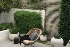 33 a modern paved patio with a planked screen, with a tiled floor, potted grasses and greenery, a small dining set with pillows and a woven chair