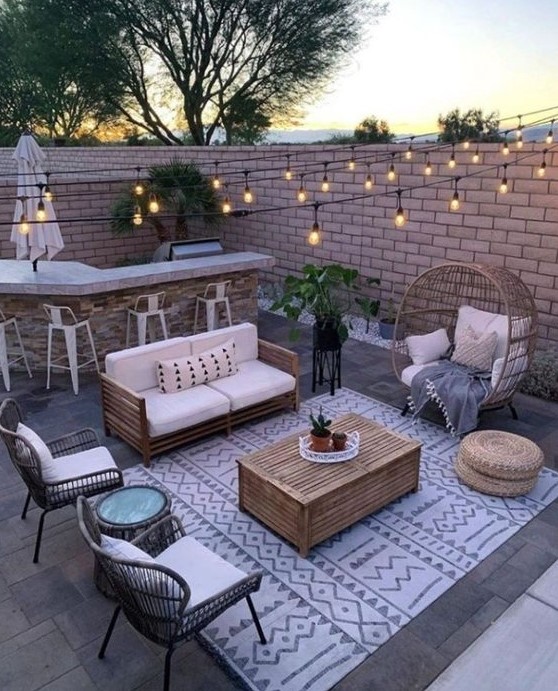a small paved patio turned into an entertainment zone, with a bar, a sitting zone with rattan furniture and string lights is very cozy