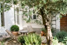 38 a small and cozy backyard with a brick clad space, some wooden chairs and lots of greenery and a tree around