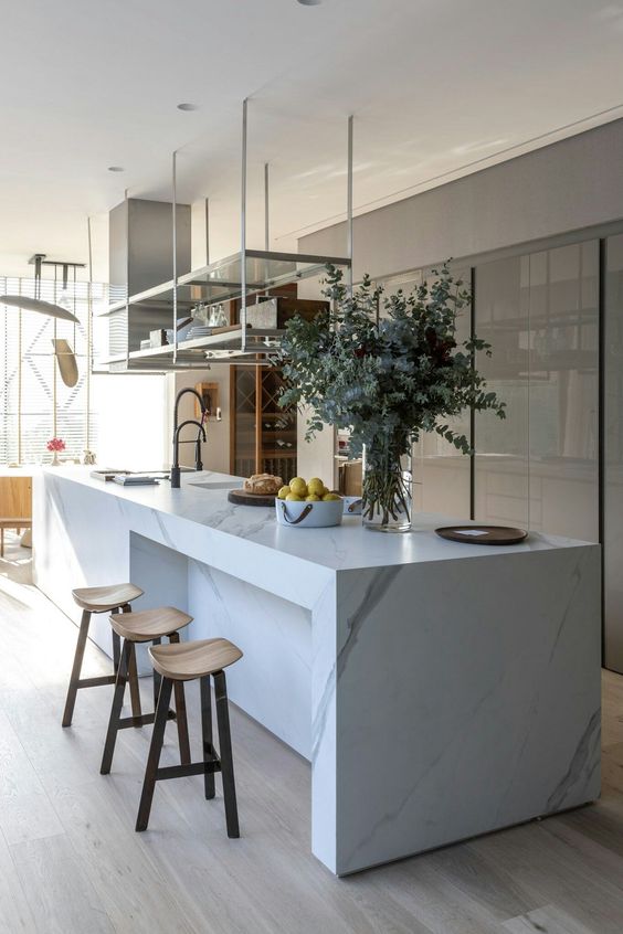 a sophisticated minimalist kitchen with a sleek grey storage unit, a white marble kitchen island, a suspended shelf