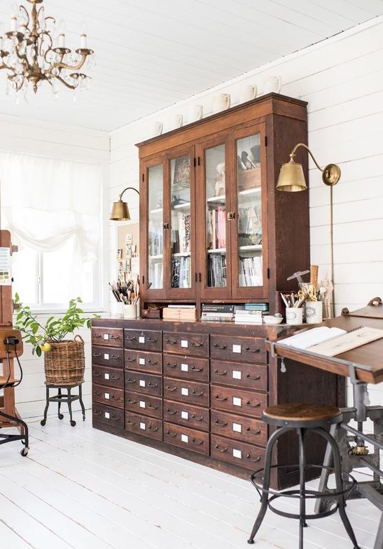 a vintage working space with a stained card cabinet and a glass one on top, a vintage industrial desk and some stools