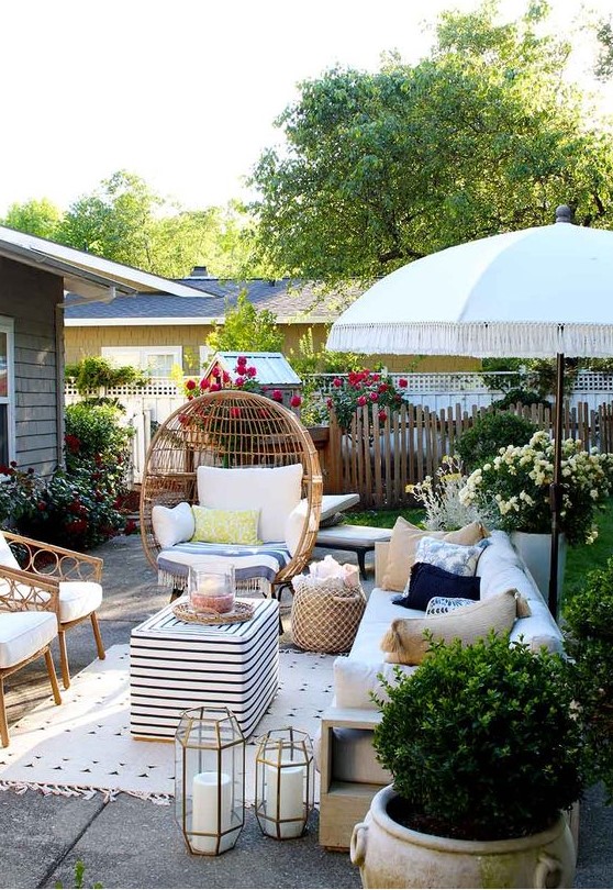 a small paved patio with rattan furniture, candles, potted greenery and bright blooms all around