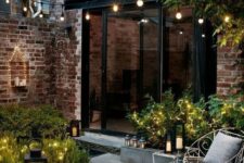 41 a tiny chic backyard clad with concrete and bricks, with greenery and lights and candle lanterns looks inviting