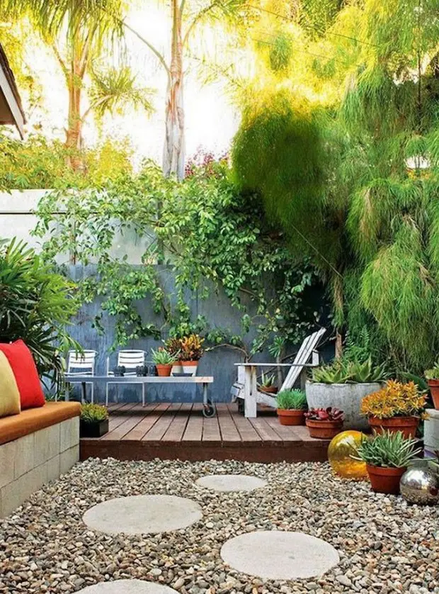 A small backyard with pebbles and a sitting zone with a built in bench, lots of potted plants, a living wall and modern garden furniture