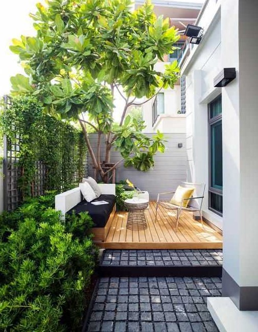 A small contemporary backyard with a wooden deck, a built in daybed and a cool chair, some growing plants and a large living tree
