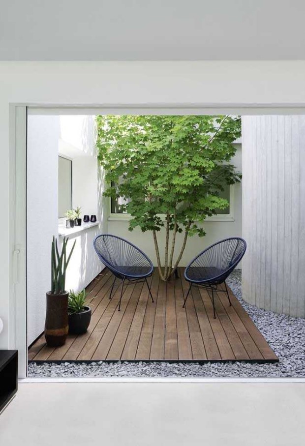 a small modern backyard with a wooden deck, navy woven chairs, a living tree and some potted plants is cool and chic