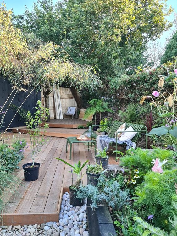 a lovely and welcoming garden with a raised wooden deck of several layers, greenery and blooms in raised garden beds