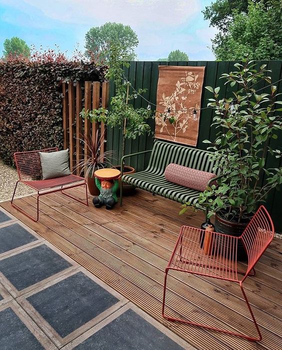 a welcoming deck with pretty and bold metal outdoor furniture, with some potted plants and a dark green fence