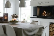 a Scandinavian dining room with a built-in fireplace and firewood storage, a table and white Panton chairs, metal pendant lamps