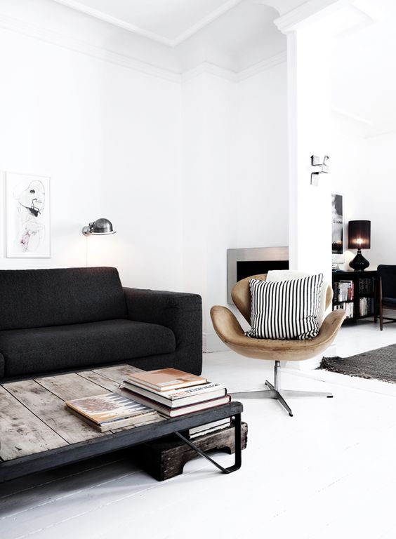 a Scandinavian living room with a black sofa, an industrial coffee table, a tan leather Swan chair and printed pillows