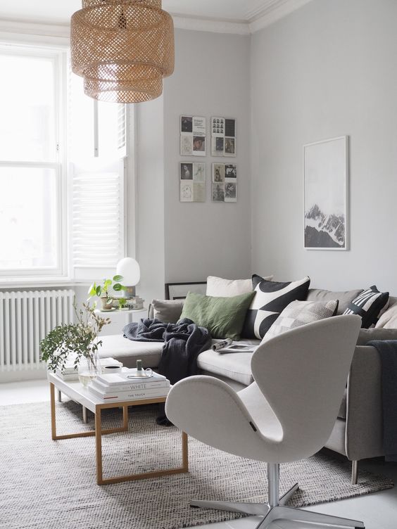 a Scandinavian living room with a grey sofa and printed pillows, a neutral Swan chair, a coffee table, artwork and a woven pendant lamp