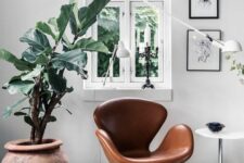 a Scandinavian space with a brown leather Swan chair, a side table, a grey daybed, a coffee table and a potted plant