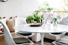 a balcony with a dining space, with a corner bench, a round table, black and white Tulp chairs and some blooms