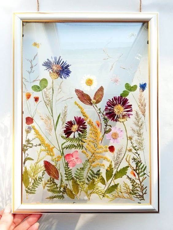a beautiful and colorful pressed flower arrangement in purple, blue and mustard, with leaves is a super chic wall art