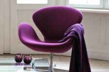 a bold and refined space with a purple Swan chair and a blanket, a coffee table with purpel glasses and a bold rug
