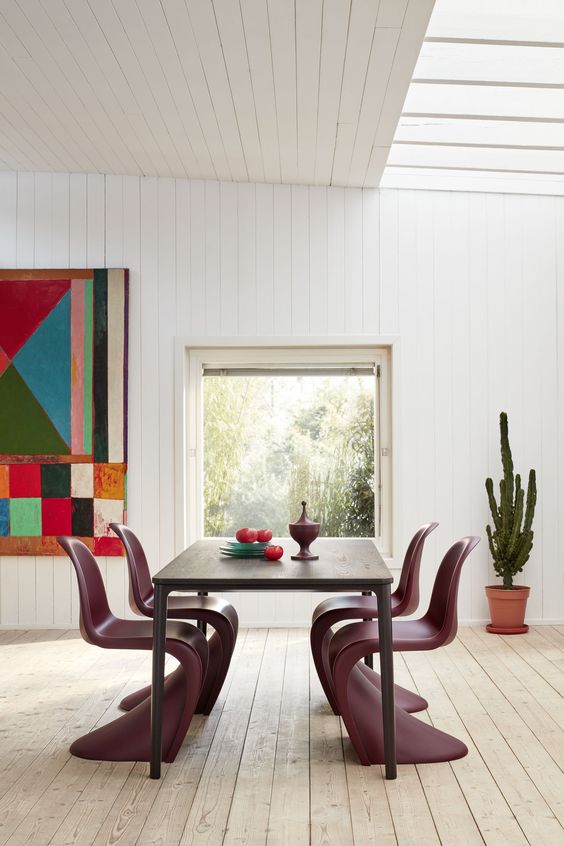 a bold dining room with a dark-stained table, purple Panton chairs, colorful art and a potted cactus is a fun and cool space