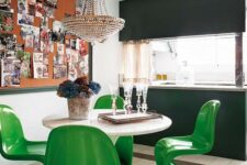 a bold dining space with a round table, bold green Panton chairs, a memo board with various photos and a crystal chandelier