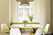 a bold dining space with a windowsill bench with mustard upholstery, a table, and mustard Tulip chairs, a pendant lamp