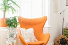 a bold nook with an orange Egg chair, a plant stand and a terrarium, a woven cat house and macrame