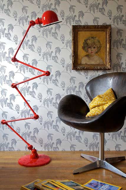 a bold space with a brown leather Swan chair and a yellow pillow, a retro folding floor lamp and an artwork