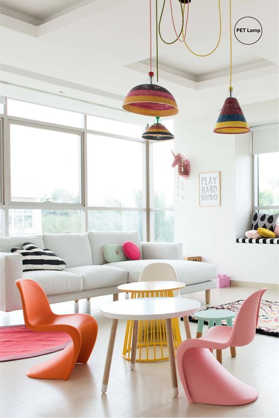 a bright space with a white sofa, some tables, colorful Panton chairs and bright striped pendant lamps and pillows