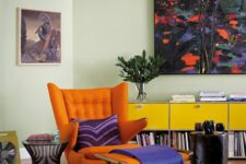 a bright space with a yellow storage unit, an orange Papa Bear chair and a footrest, a couple of side tables and bold artwork