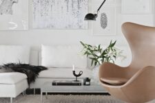 a catchy living room with a creamy corner sofa and pillows, a low coffee table, a gallery wlal and a beige leather Egg chair