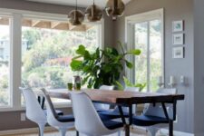 a catchy modern dining space with large windows, a stained table, navy Tulip chairs, a grey rug and pendant lamps