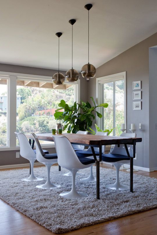 a catchy modern dining space with large windows, a stained table, navy Tulip chairs, a grey rug and pendant lamps