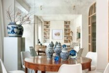 a chic dining room with a mirror accent wall, a stained table and white Tulip chairs, a storage unit with a blue vase and some vases on the table