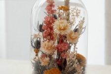 a cloche with dried flowers in pink, orange and rust, with thistles and grasses and moss is a very eye-catchy idea
