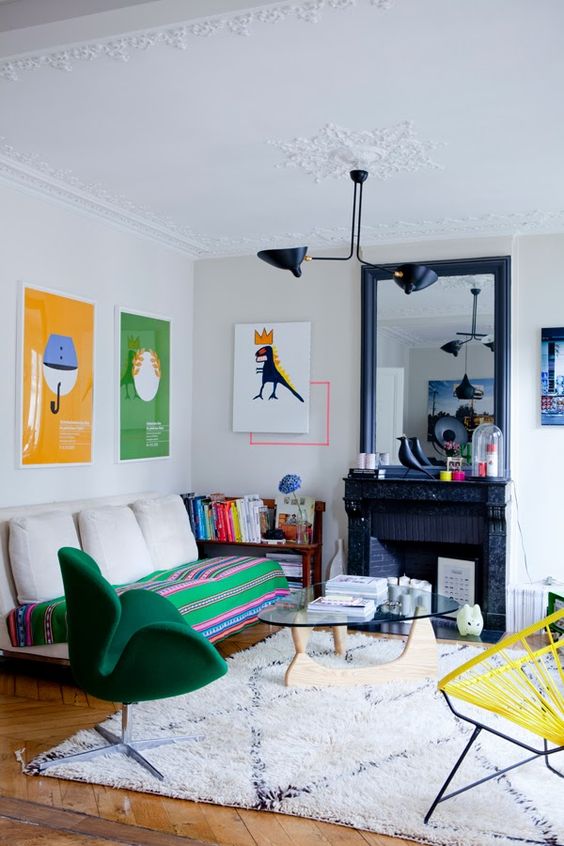 a colorful eclectic living room with a black fireplace and a mirror, a sofa with pillows, bright artwork, some decor and a green Swan chair