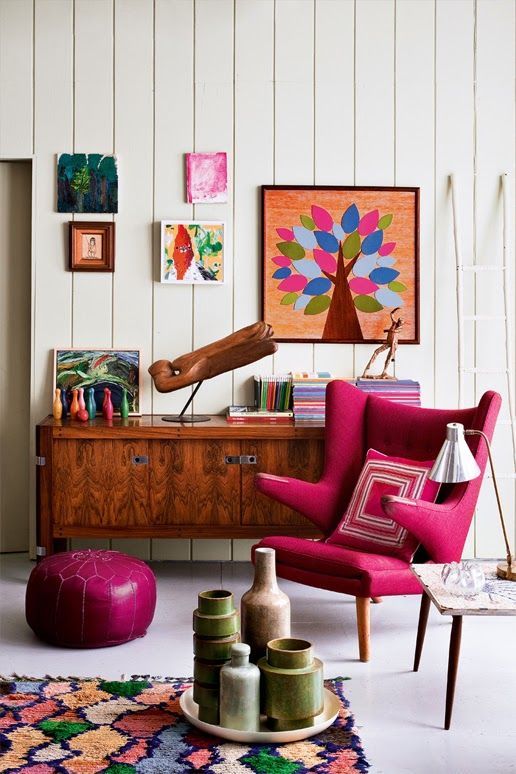 a colorful space with a rich-stained credenza, a hot pink Papa Bear chair, a printed rug, a colorful gallery wall and vases