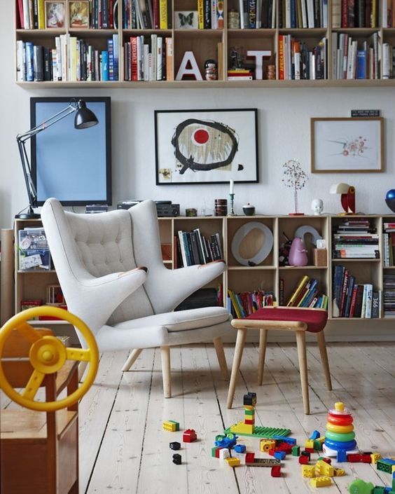 a colorful space with bookshelves and storage units, artwork, a white Papa Bear chair, a red footrest and colorful toys