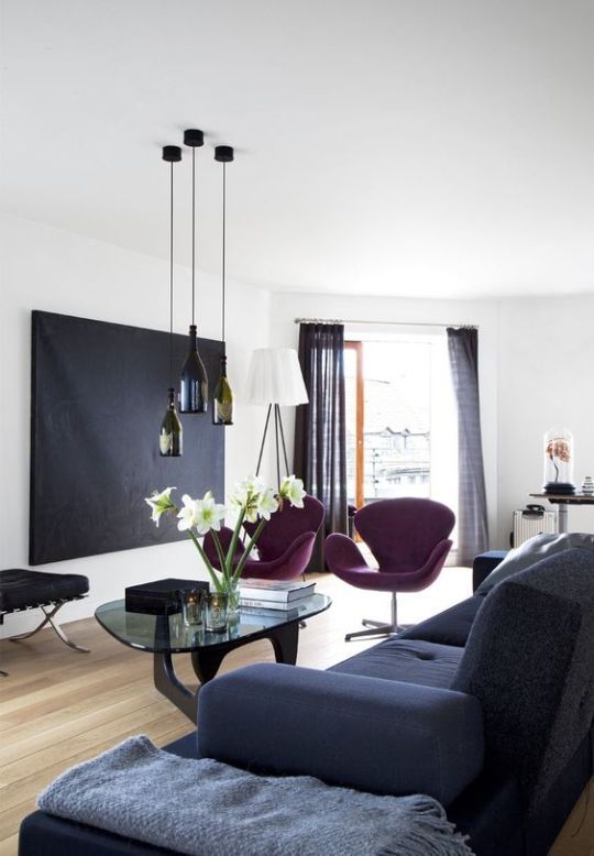 a contrasting living room with a black artwork, purple Swan chairs, bottle pendant lamps, a glass coffee table and a grey sofa