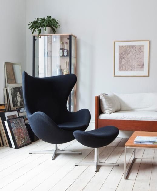 a cool Scandinavian living room with a daybed, a black Egg chair and a footrest, a coffee table and artwork, a glass storage unit